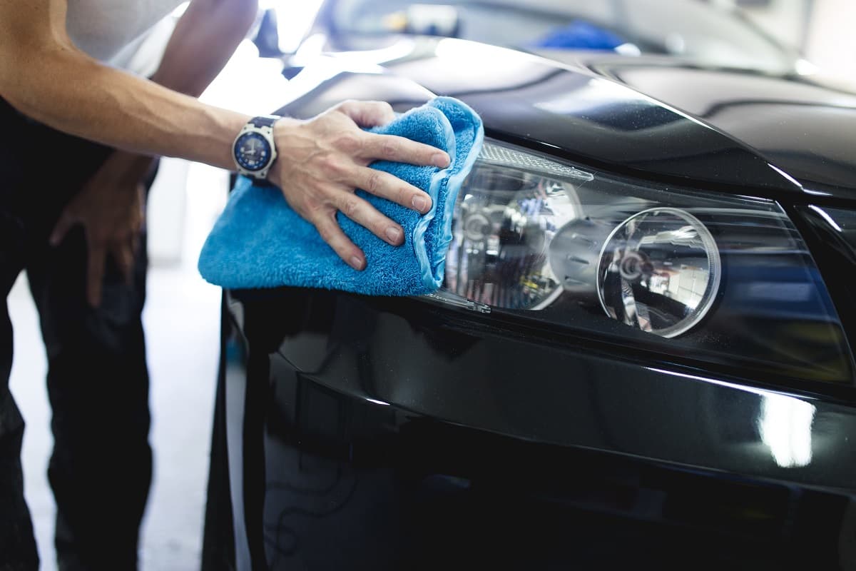 Technicien nettoyant un phare de voiture avec une microfibre
